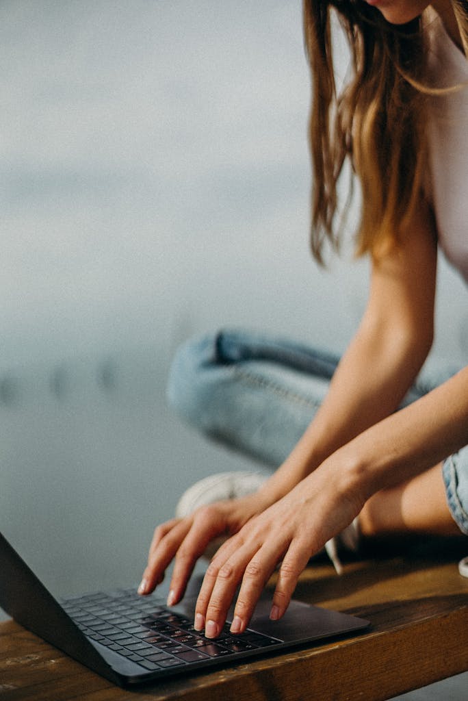 A young woman working remotely on her laptop by a calm waterfront.